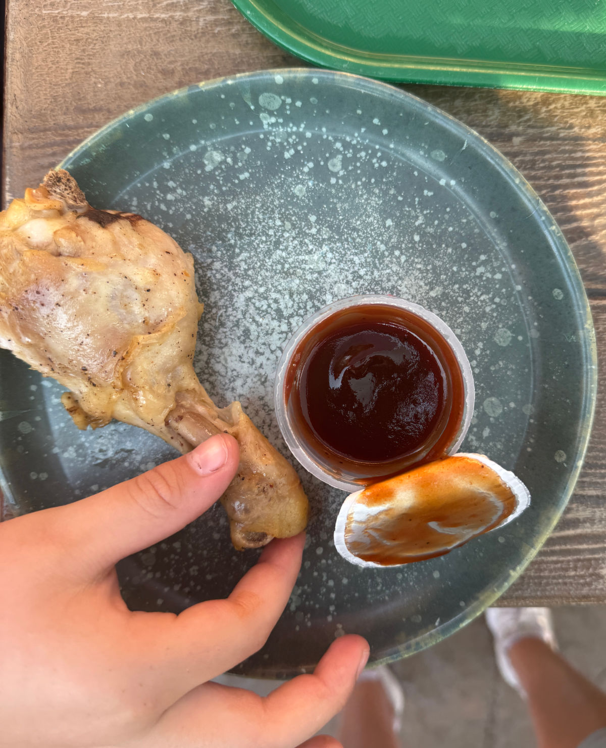 A child's hand holding a chicken drumstick on a plate.